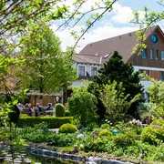 Landhaus Blumengarten: Außenansicht Üppige Gartenlandschaft mit blühenden Sträuchern umrahmt ein traditionelles Landhaus mit roten Ziegeldach.