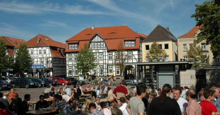 Neustadtmarktplatz Menschen versammeln sich auf einem belebten Marktplatz mit Fachwerkhäusern und Tischen unter freiem Himmel.