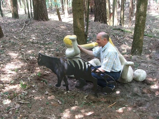 Wilhelm Wortberg Ein Mann in einem Wald sitzt nah bei einer Metallskulptur eines Höhlenlöwen und einem Knochen.