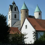 Die Busdorfkirche mit ihren zwei markanten Rundtürmen und rotem Ziegeldach bei strahlend blauem Himmel.