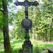 Schwarzes Kreuz Schwarzes Kreuz aus Gusseisen inmitten eines grünen Waldstücks, kunstvoll verziert mit floralen Motiven.