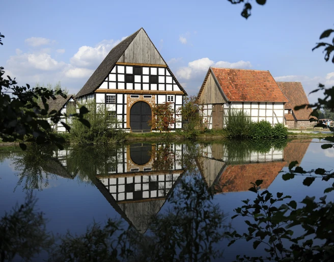 Der Dorfteich des LWL-Freilichtmuseums Detmold. Der Dorfteich im LWL-Freilichtmuseum Detmold spiegelt Fachwerkhäuser und bewölkten Himmel wider.