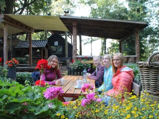 Rast an der Almhütter Vier Personen sitzen lächelnd an einem Holztisch im Freien, umgeben von bunten Blumen und Bäumen.