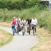 Radler Mittelweser Fünf Menschen radeln entspannt auf einem schmalen asphaltierten Weg inmitten dichter grüner Vegetation.