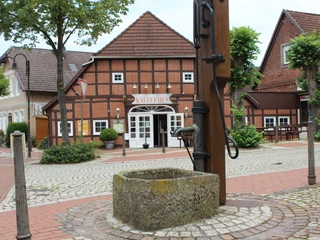 Ortsmitte Bruchhausen-Vilsen Historisches Fachwerkhaus mit Schriftzug "KAFFEEHAUS", umgeben von Pflastersteinen und Bäumen.