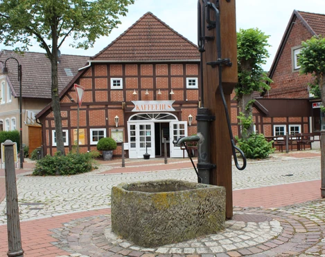 Ortsmitte Bruchhausen-Vilsen Historisches Fachwerkhaus mit Schriftzug "KAFFEEHAUS", umgeben von Pflastersteinen und Bäumen.