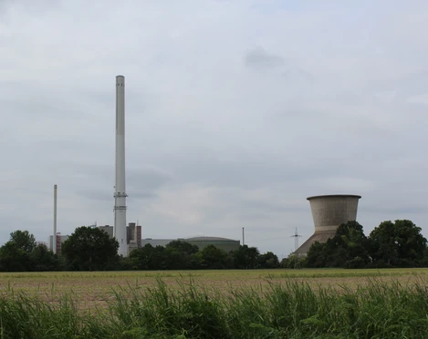 Landesbergen Kraftwerk Kraftwerk mit hohem Schornstein und Kühlturm umgeben von grünen Feldern und Bäumen an bewölktem Himmel.