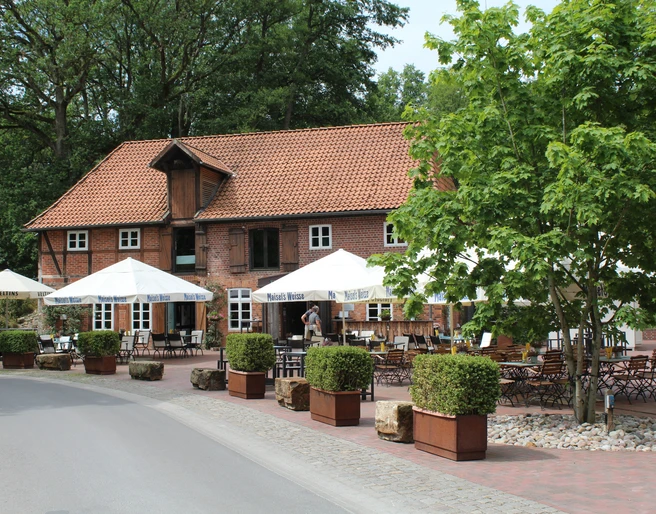 Klostermühle Heiligenberg Historische Backsteinmühle mit Biergarten, Holztischen und weißen Sonnenschirmen unter blühendem Baum.