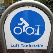 Lufttankstelle Ein Schild mit blauem Kreis und Piktogramm einer Person auf einem Fahrrad. Schrift: Luft-Tankstelle.