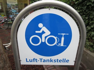 Lufttankstelle Ein Schild mit blauem Kreis und Piktogramm einer Person auf einem Fahrrad. Schrift: Luft-Tankstelle.