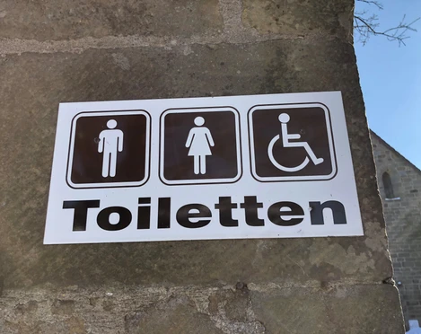 Toilettenschild am Kloster Loccum mit Symbolen für Herren, Damen und barrierefreien Zugang.