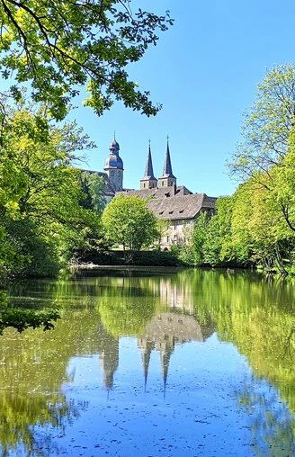 Blick auf die Abtei Marienmünster Abtei Marienmünster mit ihren markanten Türmen spiegelt sich in einem stillen, umgebenen Teich.