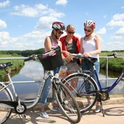 Radfahren Mittelweser Drei Radfahrer mit Helmen stehen auf einer Brücke über einem Fluss und betrachten gemeinsam eine Karte.