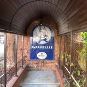 Eingang zum Jazz Keller Nienburg mit einem gewölbten Holzdach, umgeben von Backstein und grünen Pflanzen.