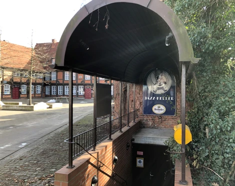 Eingang des Jazz Kellers Nienburg mit gewölbtem Dach und Treppe, umgeben von Backsteingebäuden.