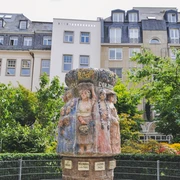 Women's fountain Der Frauenbrunnen zeigt zehn lebensgroße Frauenfiguren "die Frauen Kölns im Wandel der Zeiten“, umgeben von üppigem Grün, vor urbaner Kulisse. The Frauenbrunnen fountain shows ten life-size female figures "the women of Cologne through the ages", surrounded by lush greenery against an urban backdrop.