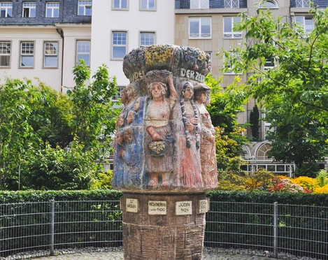 Women's fountain Der Frauenbrunnen zeigt detailreich gestaltete weibliche Figuren in traditioneller Tracht, umgeben von Natur und historischen Gebäuden.The women's fountain shows detailed female figures in traditional costume, surrounded by nature and historic buildings.