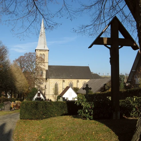 Pfarrkirche St. Margaretha mit spitzem Turm, umgeben von Bäumen und Kreuze am Friedhofsbereich.