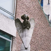 Angel statue Eine Engelsstatue aus Stein erhebt sich majestätisch an einem Gebäude aus roten Backsteinen.A stone statue of an angel rises majestically from a red brick building.