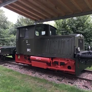 Steinhuder Meer Bahn Alte Lokomotive unter einem Schutzdach, umgeben von grünen Bäumen und auf Schienen stehend.