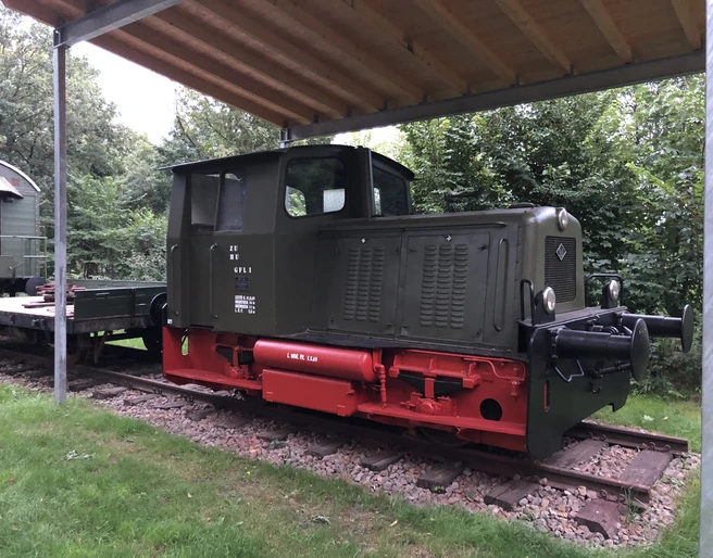Steinhuder Meer Bahn Alte Lokomotive unter einem Schutzdach, umgeben von grünen Bäumen und auf Schienen stehend.