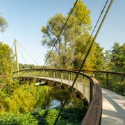 Aggerbogen Schwungvolle Holzbrücke, eingebettet in grüner Flusslandschaft unter klarem Himmel in Lohmar.