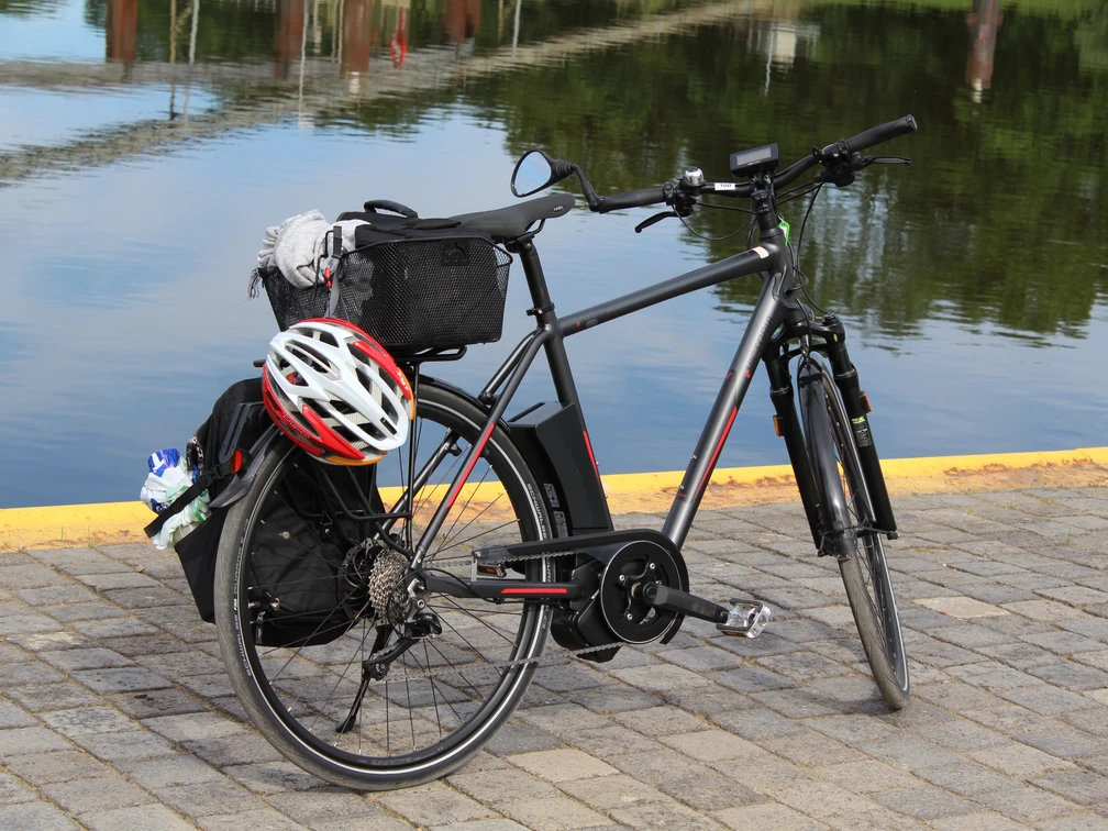 Rad Mittelweser Ein schwarzes Fahrrad mit Gepäckträger und Helm steht auf gepflastertem Boden vor ruhigem Wasser.