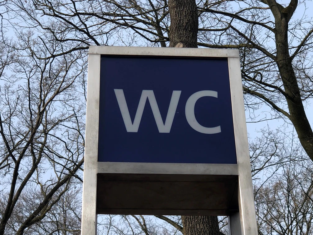 Öffentliche Toilette in einem parkähnlichen Gebiet, umgeben von Bäumen, unter freiem Himmel.