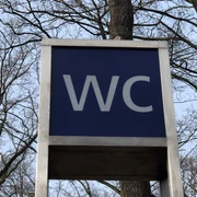 Öffentliche Toilette in einem parkähnlichen Gebiet, umgeben von Bäumen, unter freiem Himmel.