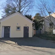 Toiletten am Bürgermeister-Stahn-Wall Öffentliche Toiletten mit zwei separaten Eingängen, umgeben von Bäumen, auf gepflastertem Boden.