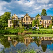 Schloss Ippenburg im Osnabrücker Land Historisches Gebäude mit Spitzgiebeln und bewachsenem Mauerwerk, Park und Teich im Vordergrund.