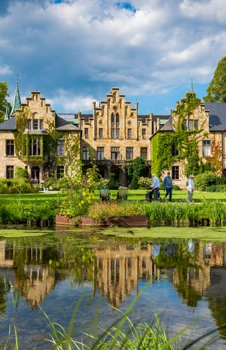 Schloss Ippenburg im Osnabrücker Land Historisches Gebäude mit Spitzgiebeln und bewachsenem Mauerwerk, Park und Teich im Vordergrund.