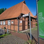 Museum Oldendorf/Luhe  Fachwerkgebäude mit rotem Ziegeldach, beschildertem Eingang zum Museum und grünem Gartenschild daneben.