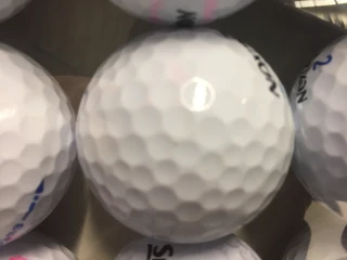 Golfbälle Nahaufnahme eines weißen Golfballs mit strukturierter Oberfläche und schwarzem Aufdruck, von sanftem Licht beleuchtet.