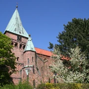 FelicianusKirche Weyhe Eine rote Backsteinkirche mit grünem Kupferturm, umgeben von Bäumen unter blauem Himmel in Weyhe.