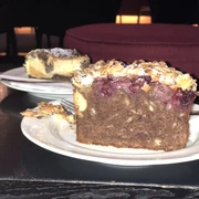 Tortenstück Ein Tortenstück auf einem weißen Teller, verziert mit Kirschen und Mandeln auf dunklem Teig.