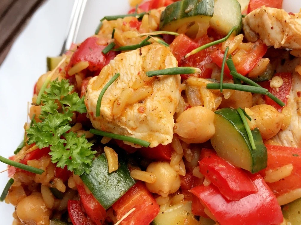 Hähnchengericht Frisches Hähnchenstück mit knackigem Paprika, Zucchini, Kichererbsen und Reis, garniert mit Schnittlauch.