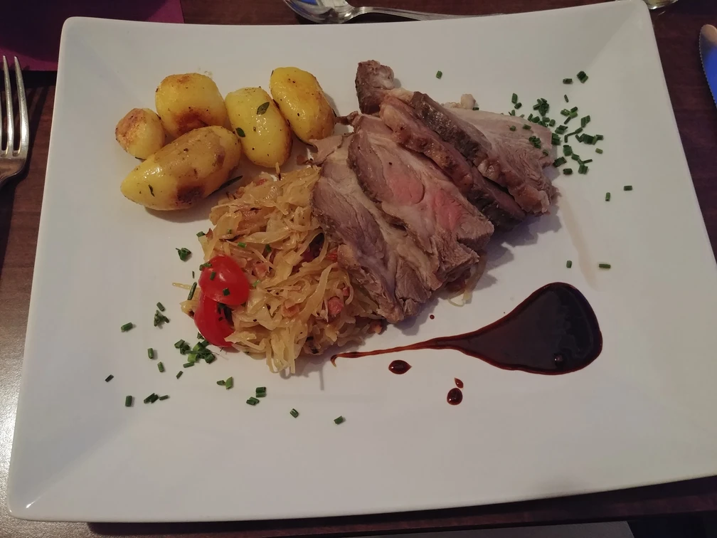 Schwein und Sauerkraut Ein Teller mit saftigen Schweinescheiben, Sauerkraut, gebratenen Kartoffeln und einem Balsamico-Tupfer.