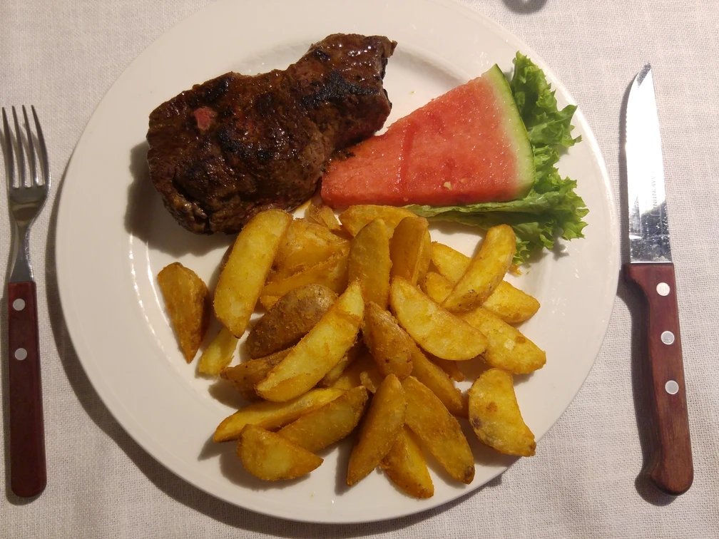 Saftiges Steak mit frisch goldenen Kartoffelspalten und erfrischender Wassermelone auf einem Teller.