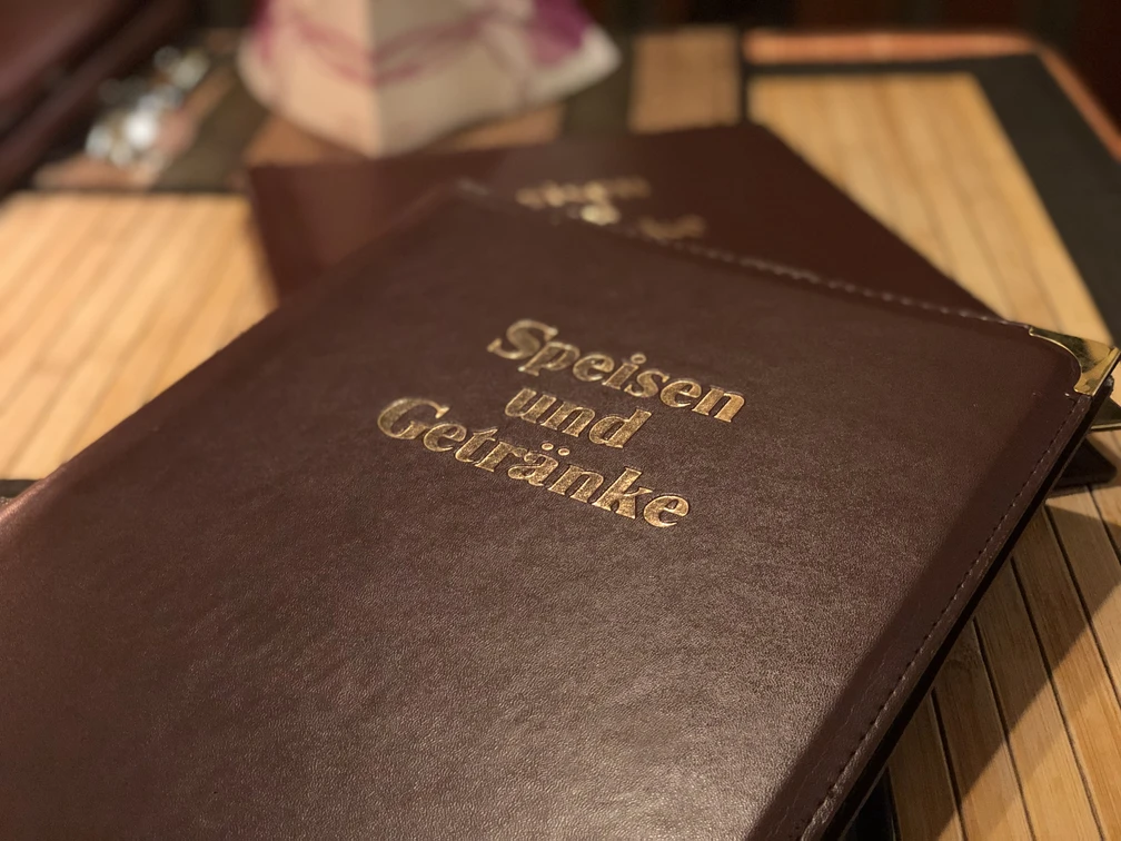 Nahaufnahme eines dunkelbraunen Leder-Speisekartenordners mit goldener Prägung "Speisen und Getränke".