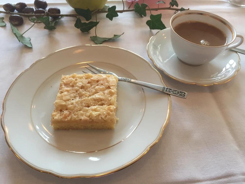 Kaffee + Kuchen Ein fein gedeckter Tisch mit einem Stück Kuchen auf einem Teller und einer Tasse Kaffee daneben.