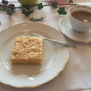 Kaffee + Kuchen Ein fein gedeckter Tisch mit einem Stück Kuchen auf einem Teller und einer Tasse Kaffee daneben.