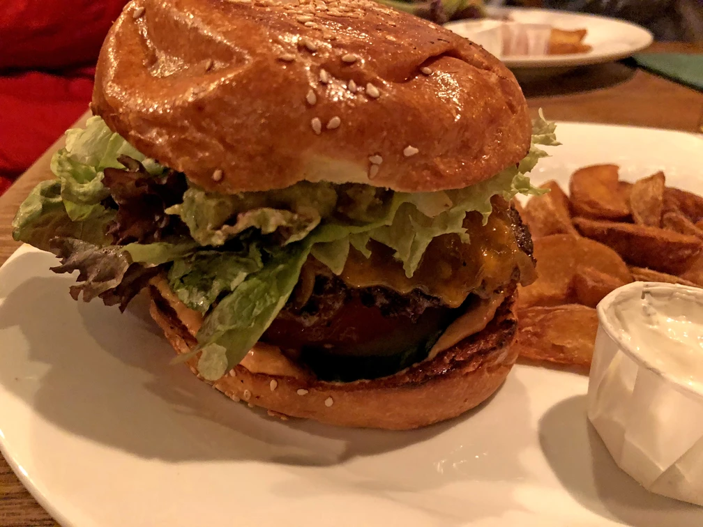Burger  Burger auf Sesambrötchen mit Salatblatt, Käse und Beilage auf einem weißen Teller arrangiert.