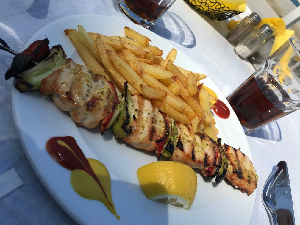 Fleischspieß Gegrillter Fleischspieß mit Paprika und Zwiebeln, serviert mit Pommes frites und Limonenviertel.