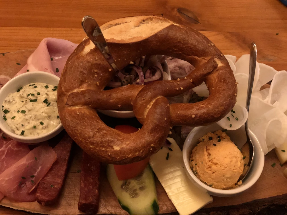 Brezel Herzhafte Brotzeitplatte mit Brezel, regionalen Aufschnitten und Käse, begleitet von würzigen Dips.