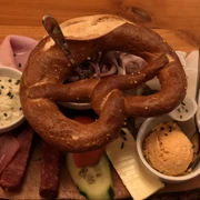 Brezel Herzhafte Brotzeitplatte mit Brezel, regionalen Aufschnitten und Käse, begleitet von würzigen Dips.