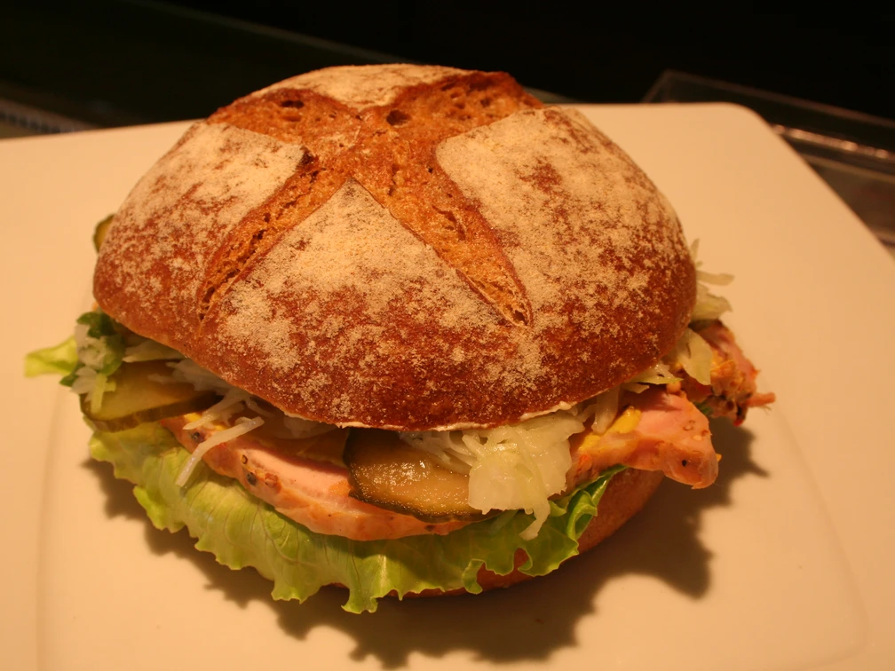 Belegtes Brötchen Ein belegtes Vollkornbrötchen mit frischem Salat, Gewürzgurke, Krautsalat und Schinken auf einem Teller.