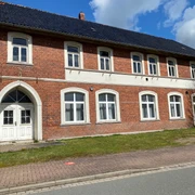 Neues von Uhlenbusch Haus Loccum Zweistöckiges Backsteingebäude mit weißen Fenstern und Türen, umgeben von einer Wiese und Gehweg.