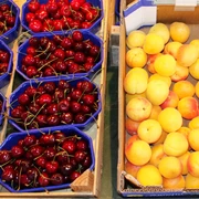 Wochenmarkt Uchte Frische rote Kirschen und reife gelbe Aprikosen in Behältern auf einem Marktstand bei Tageslicht.