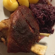 Haxe Knusprige Schweinshaxe mit goldbrauner Kruste, serviert mit Kartoffeln und Rotkohl auf weißem Teller.